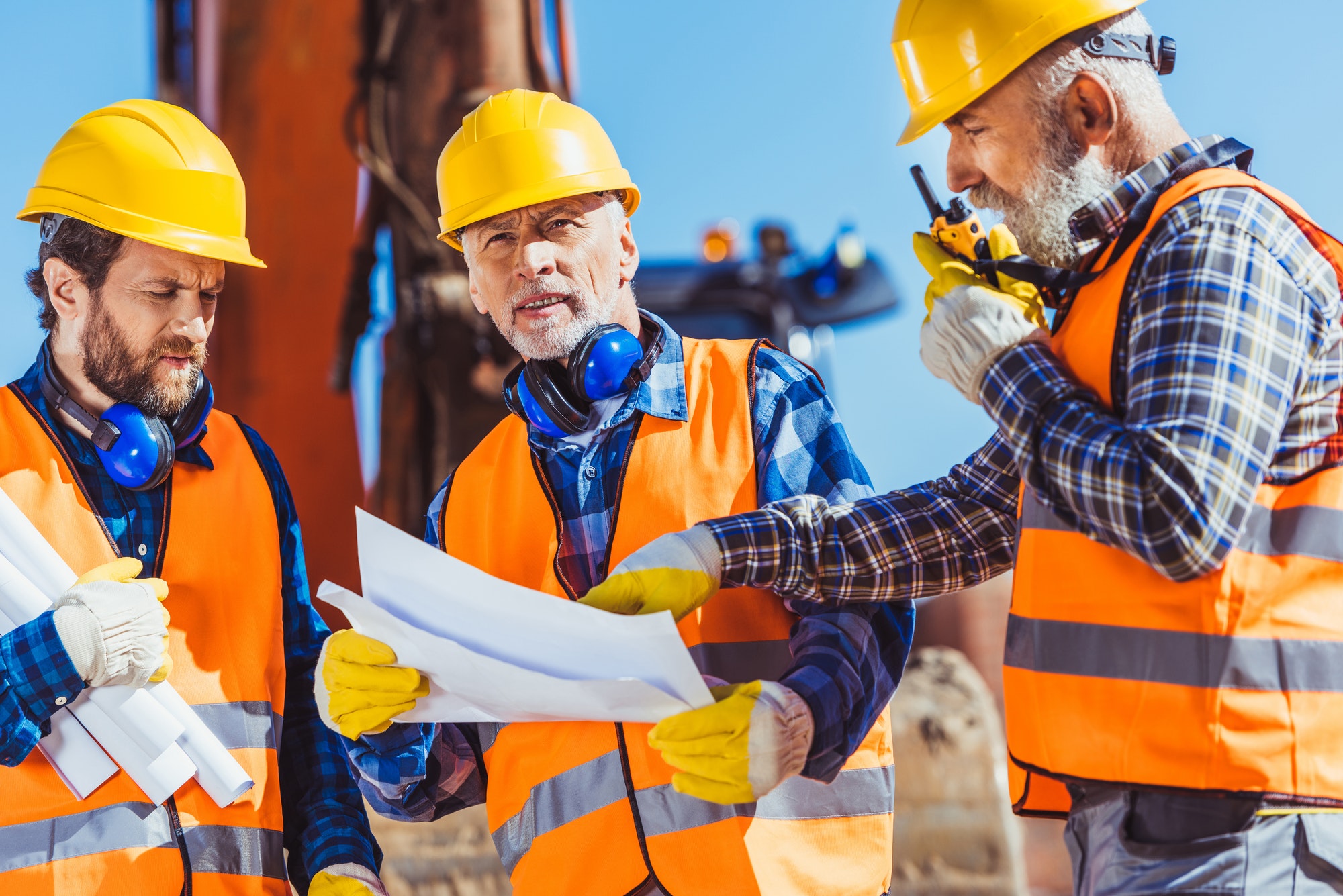 three workers examining building plans and talking on portable radio at construction site